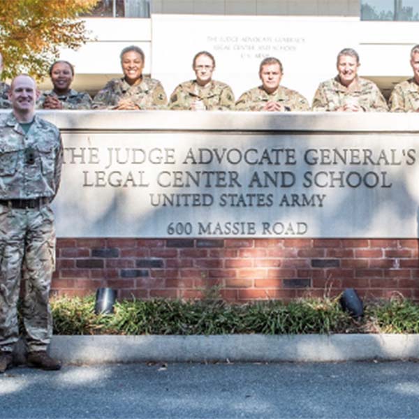 Soldiers standing in front of the TJAGLCS building sign